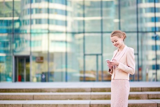 Young confident business woman in modern glass office interior using the mobile phone