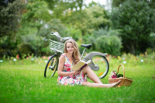 Beautiful young girl with bicycle in the countryside, reading a book