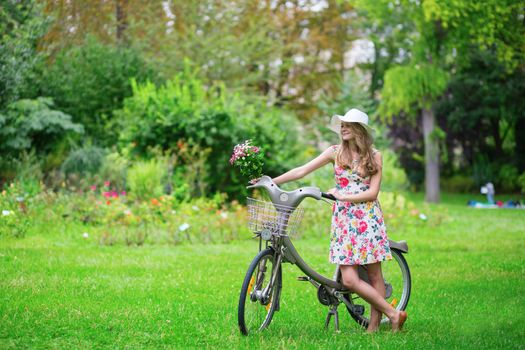 Happy young girl with bicycle and flowers in countryside on a summer day 