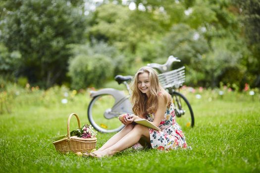 Beautiful young girl with bicycle in the countryside, reading a book
