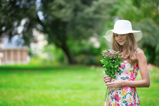 Young girl in white hat holding bunch of flowers