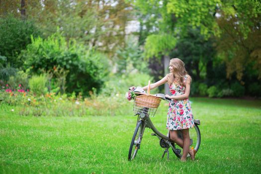 Happy young girl with bicycle and flowers in countryside on a summer day 
