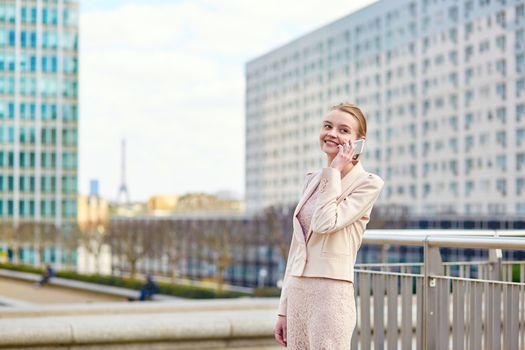 Young confident business woman in Paris using the mobile phone, Eiffel tower is in the background