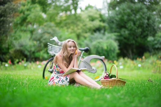 Young girl sitting on the grass and reading a book in the countryside