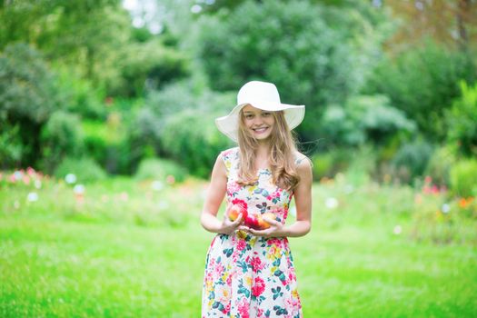 Beautiful young girl in white hat holding apples