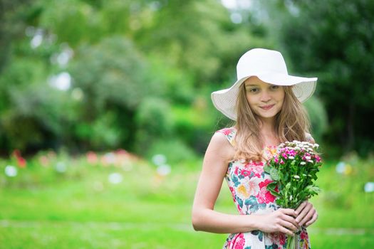 Beautiful young girl in white hat holding flowers