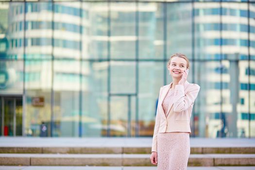 Young confident business woman in modern glass office interior  speaking on the mobile phone
