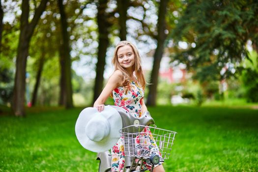 Happy young girl with bicycle and flowers in countryside on a summer day