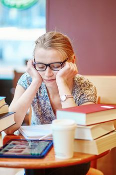 Beautiful young student with lots of books, studying or preparing for exams in a cafe. Shallow DOF