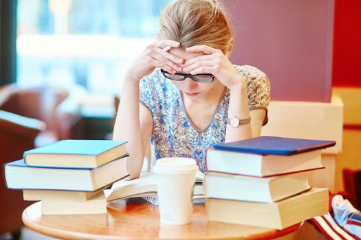 Beautiful young student with lots of books, studying or preparing for exams in a cafe. Shallow DOF