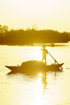 Vietnamese woman rowing wooden boat on river at sunset