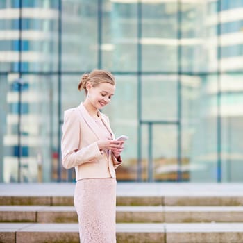 Young confident business woman in modern glass office interior using the mobile phone
