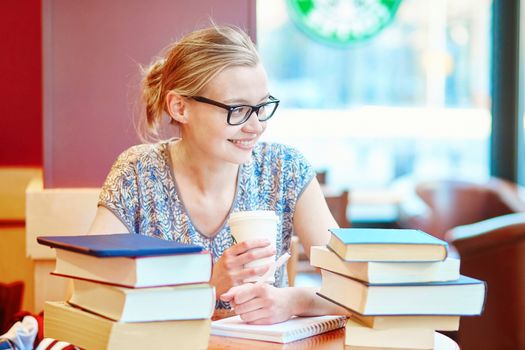 Beautiful young student with lots of books, studying or preparing for exams in a cafe. Shallow DOF