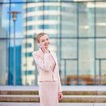 Young confident business woman in modern glass office interior using the mobile phone