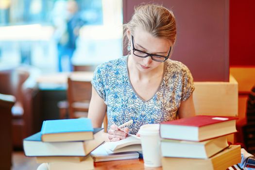 Beautiful young student with lots of books, studying or preparing for exams in a cafe. Shallow DOF