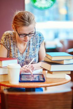 Beautiful young student with lots of books, studying or preparing for exams in a cafe. Shallow DOF