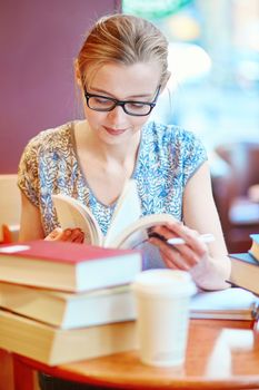 Beautiful young student with lots of books, studying or preparing for exams in a cafe. Shallow DOF