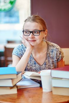 Beautiful young student with lots of books, studying or preparing for exams in a cafe. Shallow DOF