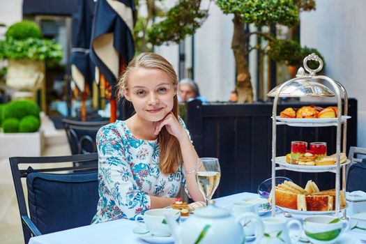 Beautiful young woman enjoying afternoon tea with selection of fancy cakes and sandwiches in a luxury Parisian restaurant