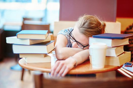 Beautiful young student with lots of books, preparing for exams in a cafe and sleeping on the table tired. Shallow DOF