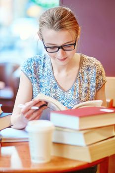 Beautiful young student with lots of books, studying or preparing for exams in a cafe. Shallow DOF