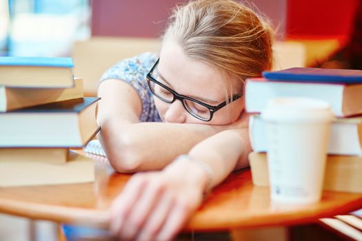 Beautiful young student with lots of books, sleeping on the table, tired of preparing for exams. Shallow DOF