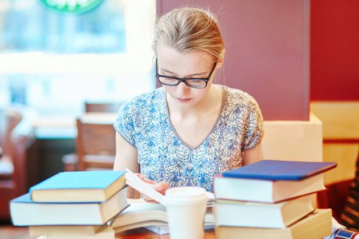 Beautiful young student with lots of books, studying or preparing for exams in a cafe. Shallow DOF