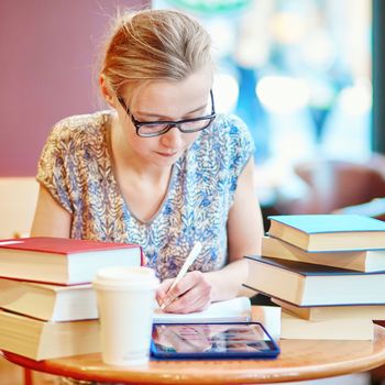 Beautiful young student with lots of books, studying or preparing for exams in a cafe. Shallow DOF