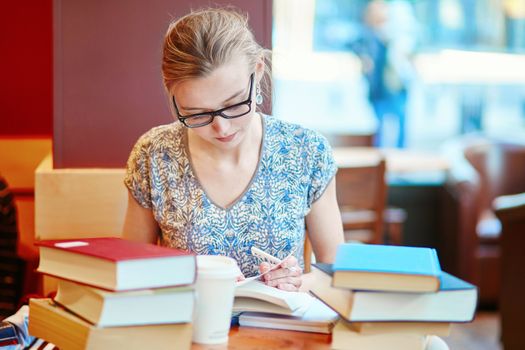 Beautiful young student with lots of books, studying or preparing for exams in a cafe. Shallow DOF