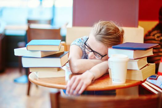Beautiful young student with lots of books, sleeping on the table, tired of preparing for exams. Shallow DOF