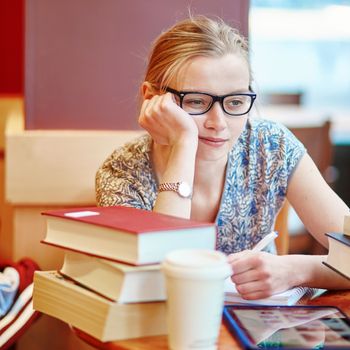 Beautiful young student with lots of books, studying or preparing for exams in a cafe. Shallow DOF