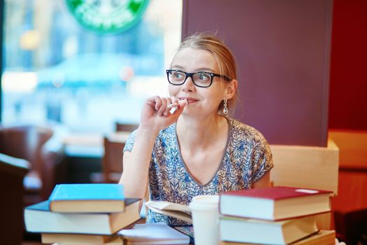 Beautiful young student with lots of books, studying or preparing for exams in a cafe. Shallow DOF