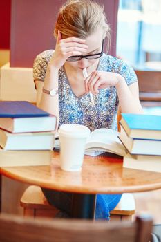 Beautiful young student with lots of books, studying or preparing for exams in a cafe. Shallow DOF
