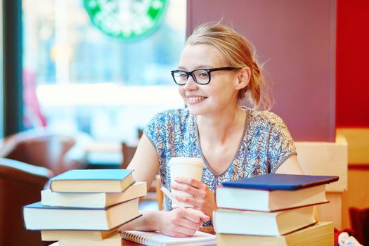 Beautiful young student with lots of books, studying or preparing for exams in a cafe. Shallow DOF