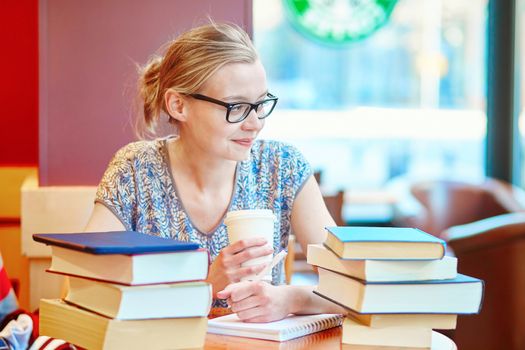 Beautiful young student with lots of books, studying or preparing for exams in a cafe. Shallow DOF