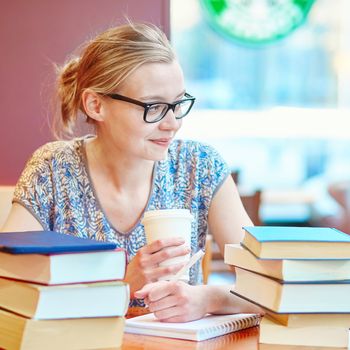 Beautiful young student with lots of books, studying or preparing for exams in a cafe. Shallow DOF