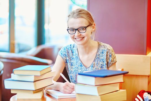 Beautiful young student with lots of books, studying or preparing for exams in a cafe. Shallow DOF