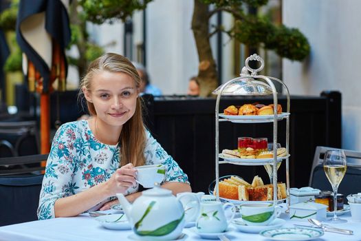 Beautiful young woman enjoying afternoon tea with selection of fancy cakes and sandwiches in a luxury Parisian restaurant