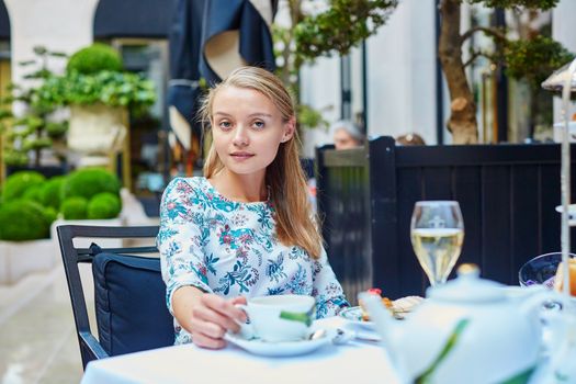 Beautiful young woman enjoying afternoon tea with selection of fancy cakes and sandwiches in a luxury Parisian restaurant
