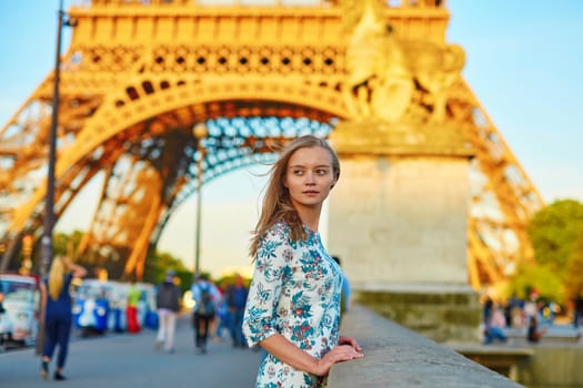 Young beautiful and elegant Parisian woman in blue dress near the Eiffel tower in Paris