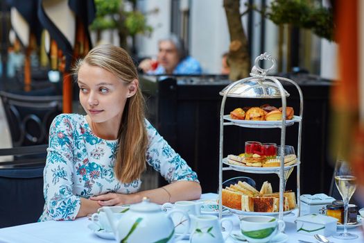 Beautiful young woman enjoying afternoon tea with selection of fancy cakes and sandwiches in a luxury Parisian restaurant