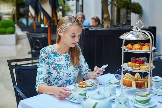 Beautiful young woman enjoying afternoon tea with selection of fancy cakes and sandwiches in a luxury Parisian restaurant