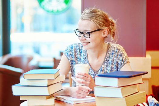 Beautiful young student with lots of books, studying or preparing for exams in a cafe. Shallow DOF