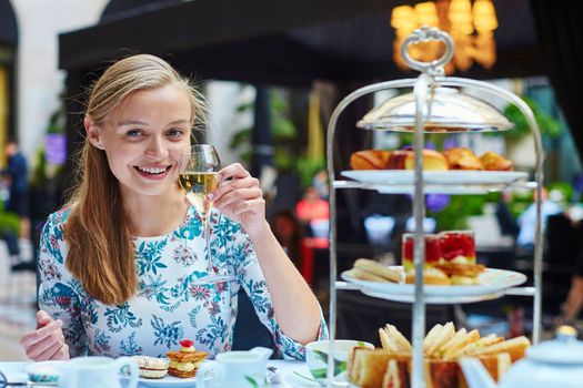 Beautiful young woman enjoying afternoon tea with selection of fancy cakes and sandwiches in a luxury Parisian restaurant