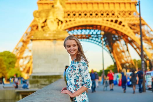 Young beautiful and elegant Parisian woman in blue dress near the Eiffel tower in Paris