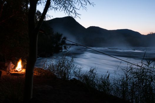 A campfire at sunset next to the Kunene River at the top of the Epupa waterfalls