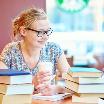 Beautiful young student with lots of books, studying or preparing for exams in a cafe. Shallow DOF