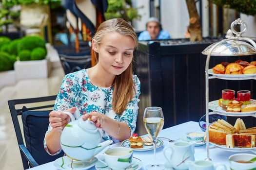 Beautiful young woman enjoying afternoon tea with selection of fancy cakes and sandwiches in a luxury Parisian restaurant