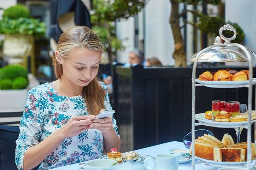 Beautiful young woman enjoying afternoon tea with selection of fancy cakes and sandwiches in a luxury Parisian restaurant