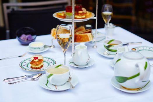 Beautiful table setting with selection of sandwiches, fancy cakes, tea and champagne served for the ceremony of afternoon tea
